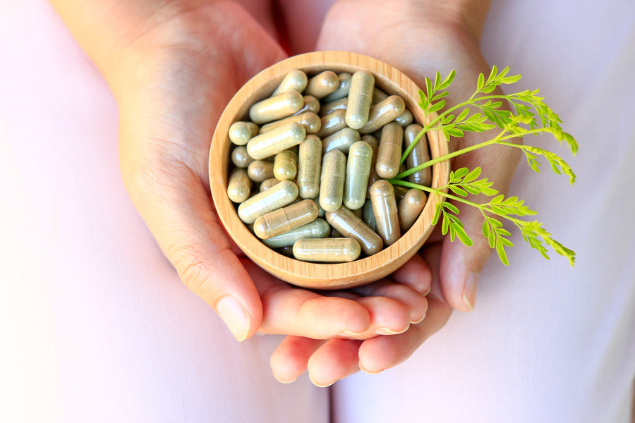 Handen met een houten kom vol capsules met voedingssupplementen